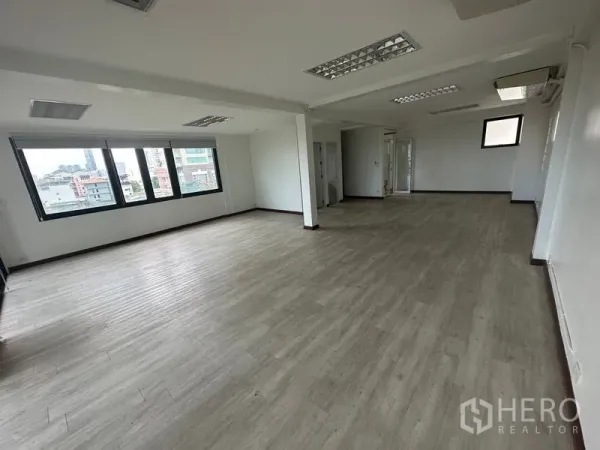 办公空间 出租在Sathon, Bangkok - 宽敞写字楼楼层，大片窗户俯瞰天际线，浅色墙面，荧光灯照明，结构立柱，并设有卫生间与杂物区入口。