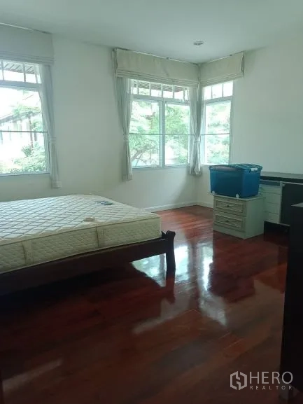 Detached House for rent in Bang Rak, Bangkok - Bright bedroom with large corner windows and polished wood flooring.