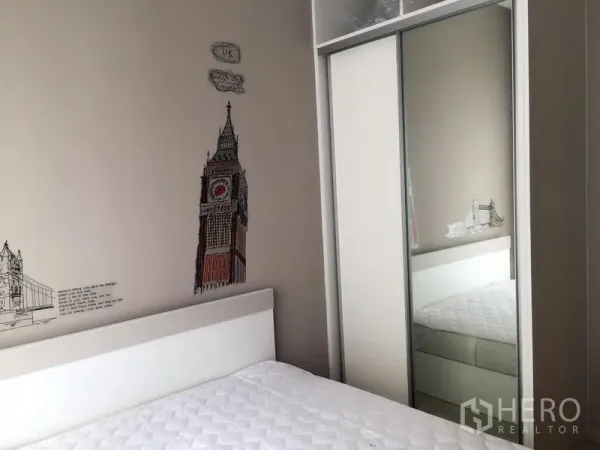 Condominium for sale in Huai Khwang, Bangkok - Compact bedroom with London-themed wall art, white bed, and mirrored sliding wardrobe.