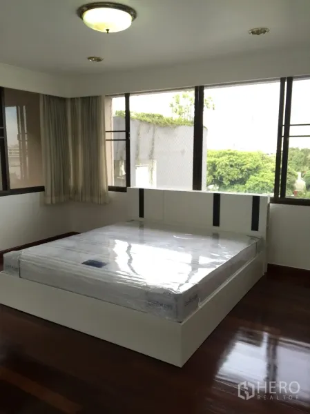 Condominium for rent or sale in Watthana, Bangkok - Bright corner bedroom with large windows and polished hardwood floors.