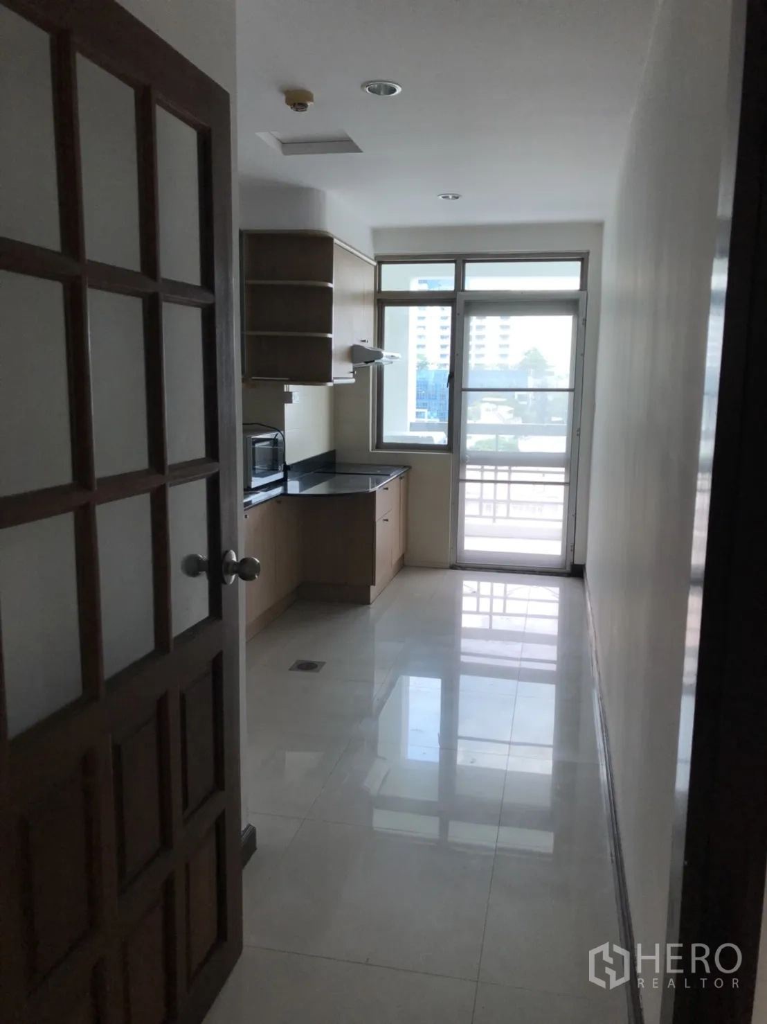 Condominium for rent in Watthana, Bangkok - Corridor leading to a bright kitchen with balcony door.