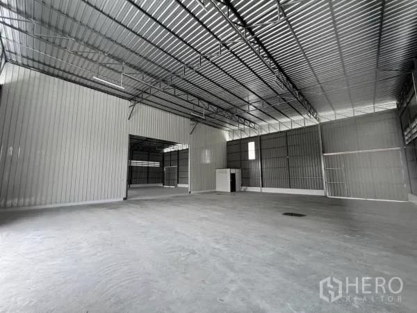 Warehouse for rent in Lam Luk Ka, Pathum Thani - Spacious warehouse interior with high steel truss roof, concrete floor and a partitioned utility core.