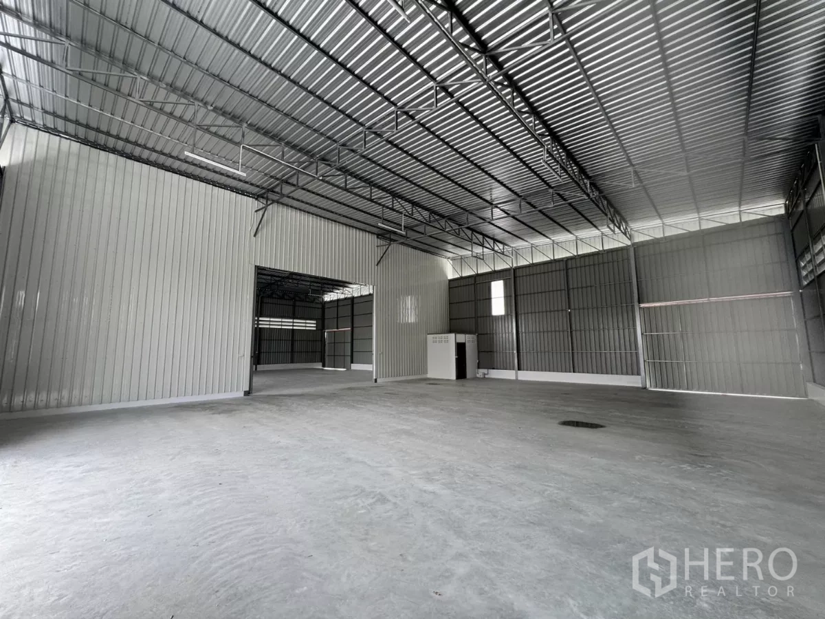 Warehouse for rent in Lam Luk Ka, Pathum Thani - Spacious warehouse interior with high steel truss roof, concrete floor and a partitioned utility core.