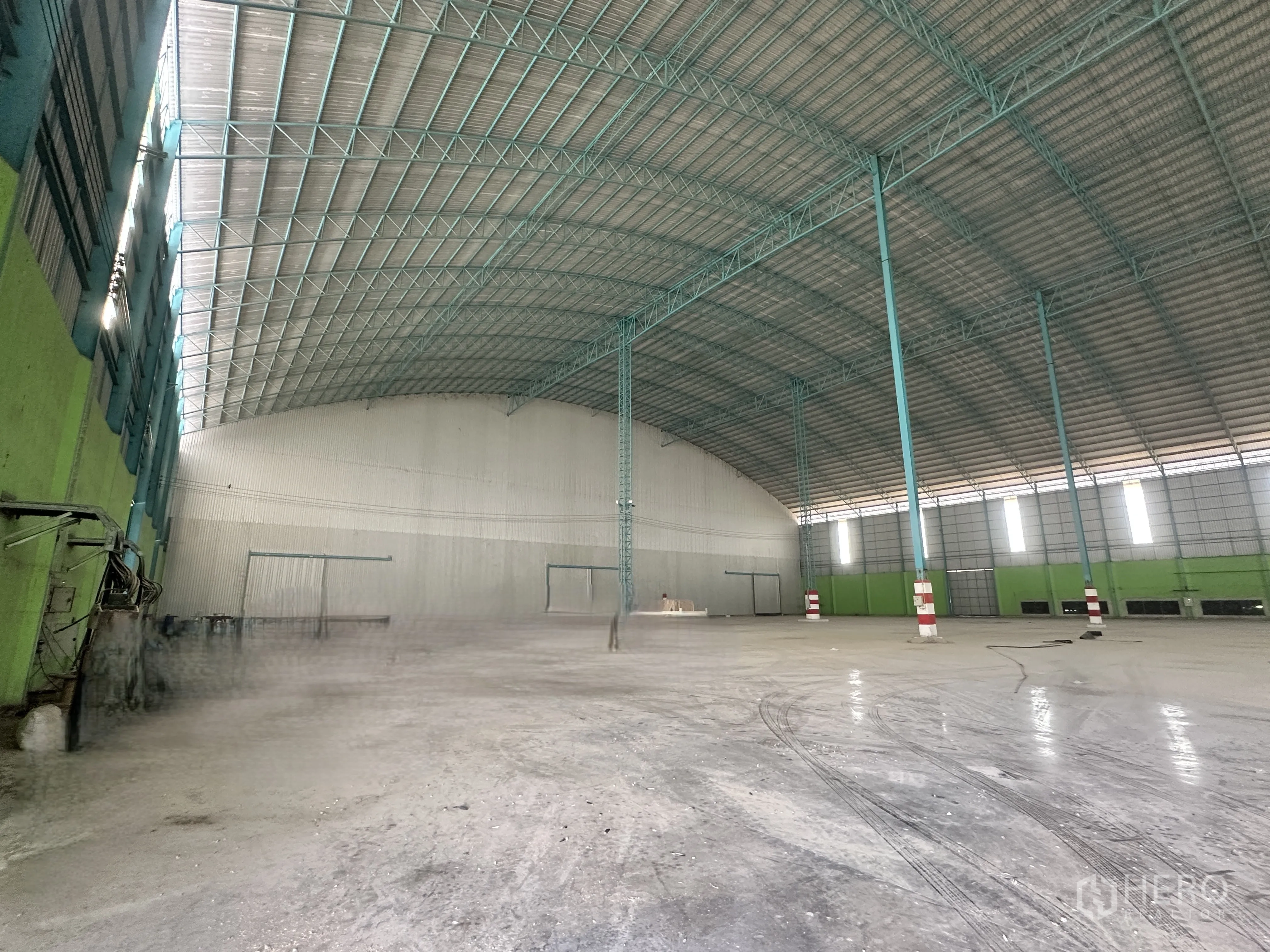 Warehouse for rent in Sai Noi, Nonthaburi - Vast warehouse interior with high arched metal roof, open concrete floor, steel columns, and roller shutter doors.