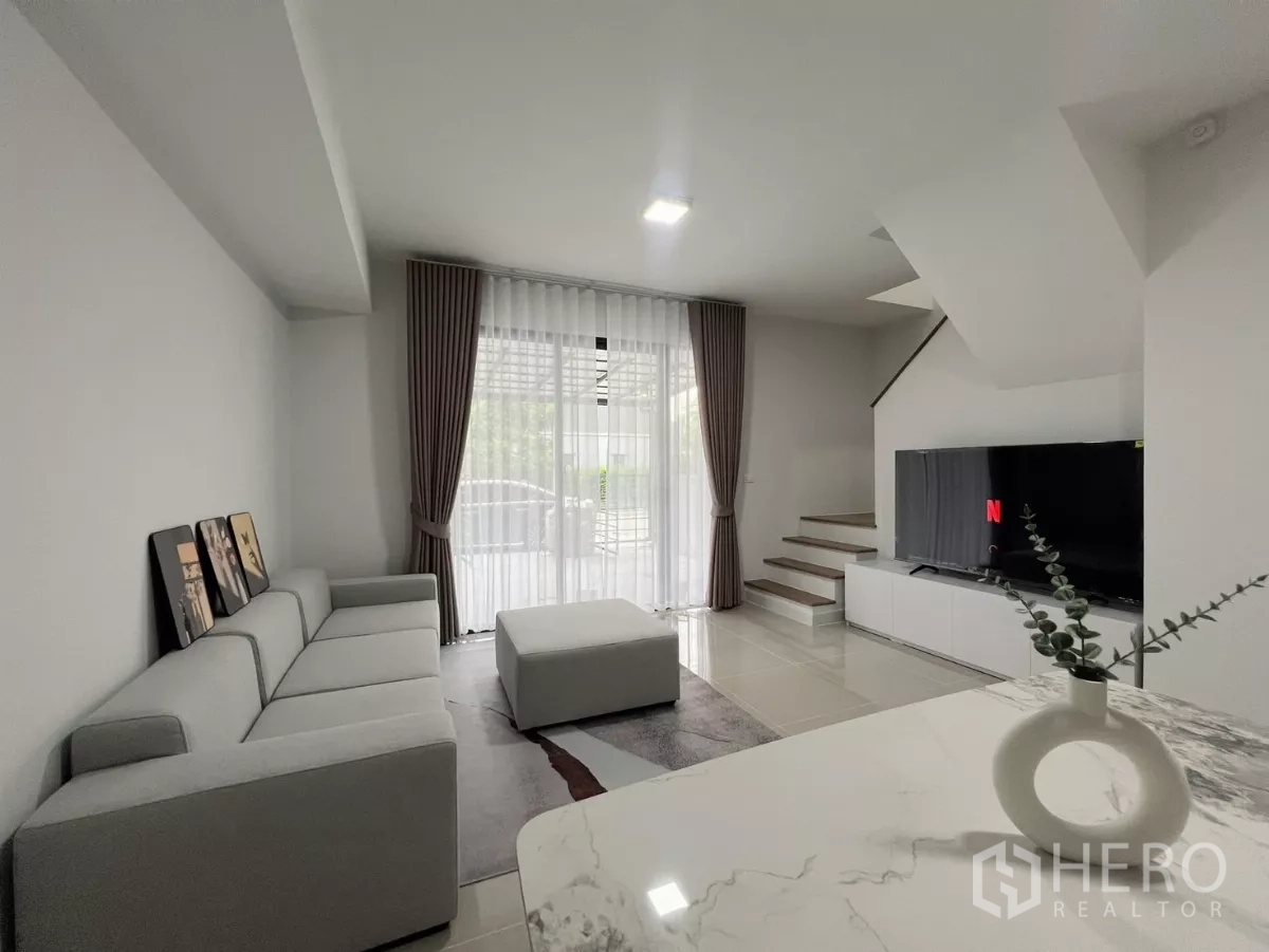 Townhouse for rent in Bang Phli, Samut Prakan - Open-plan lounge with sofa, ottoman, TV unit and staircase facing the front patio.