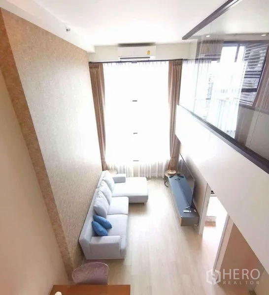 公寓 出租在Sathon, Bangkok - 阁楼式客厅，双层挑高与整面窗帘，从夹层俯视视角。