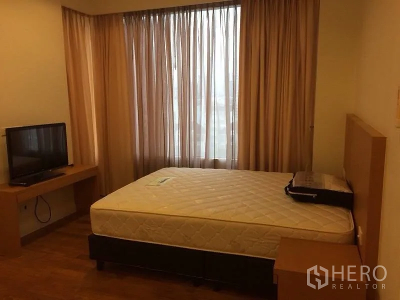 Condominium for rent in Watthana, Bangkok - Cozy bedroom with large window and sheer curtains, TV on wooden desk, and a double bed.