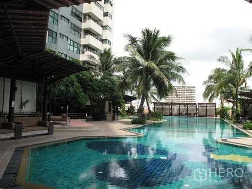 Condominium for rent in Sathon, Bangkok - Outdoor swimming pool with palm trees and shaded seating areas.