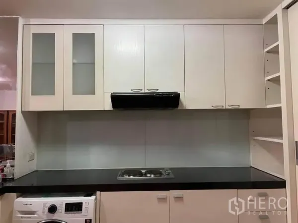 公寓 出租或出售在Watthana, Bangkok - 现代白色厨房，玻璃吊柜、电炉、抽油烟机及室内洗衣机。