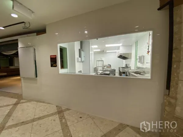 Retail Space for rent - Viewing window into a commercial kitchen with white tiles and stainless-steel equipment.
