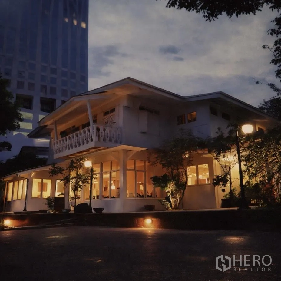 Retail Space for rent in Watthana, Bangkok - Evening exterior of an illuminated two‑storey retail house with balcony and wraparound windows set amid city towers.
