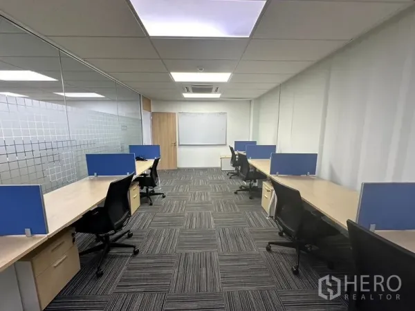 Office Space for rent - Enclosed team room with glass partition, long desks, blue screens, task chairs and a whiteboard.