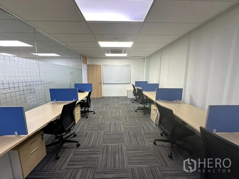 Office Space for rent - Enclosed team room with glass partition, long desks, blue screens, task chairs and a whiteboard.