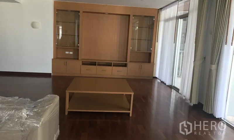 房间 出租在Watthana, Bangkok - 客厅内置木质展示柜与茶几，旁边是阳台落地门。