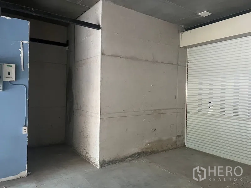 Retail Space for rent in Khlong Toei, Bangkok - Interior corner of the shop showing a partitioned back area, utility panel and a closed shutter door.