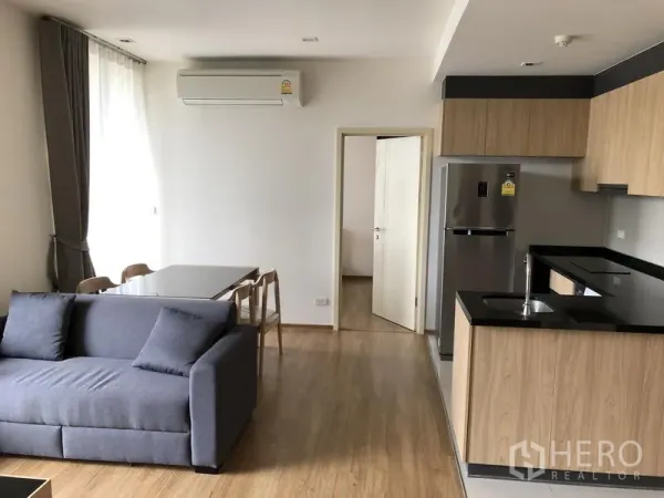 Condominium for rent in Watthana, Bangkok - Dining nook beside large window and U‑shaped kitchen with stainless refrigerator and sink.