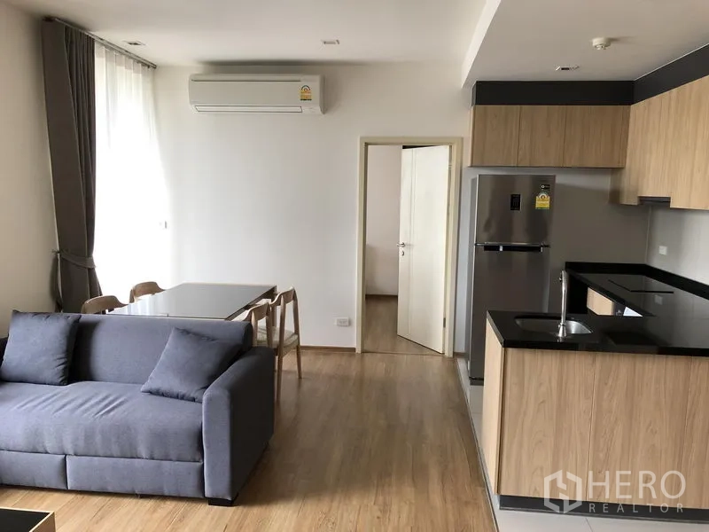 Condominium for rent in Watthana, Bangkok - Dining nook beside large window and U‑shaped kitchen with stainless refrigerator and sink.