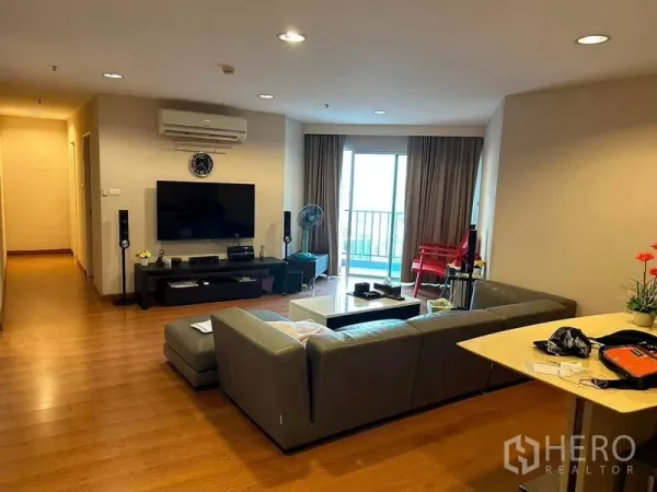 คอนโด ขายในHuai Khwang, Bangkok - ห้องนั่งเล่นกว้าง โซฟา L-shape ชุดวางทีวี และประตูกระจกบานเลื่อนออกสู่ระเบียง