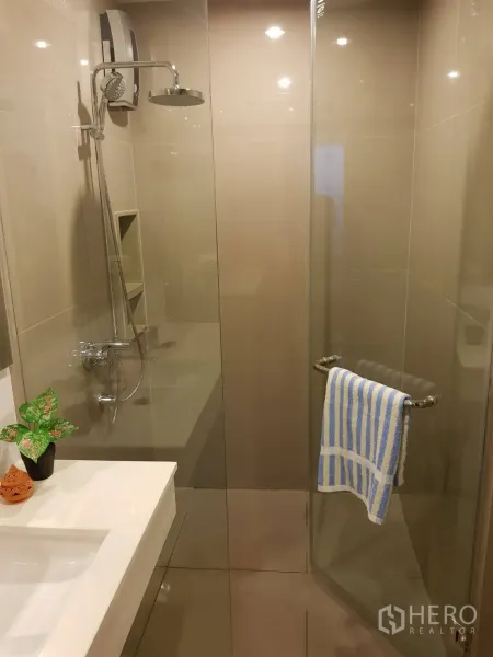 Condominium for rent in Khlong Toei, Bangkok - Modern bathroom featuring a glass-enclosed rain shower and sleek white vanity.