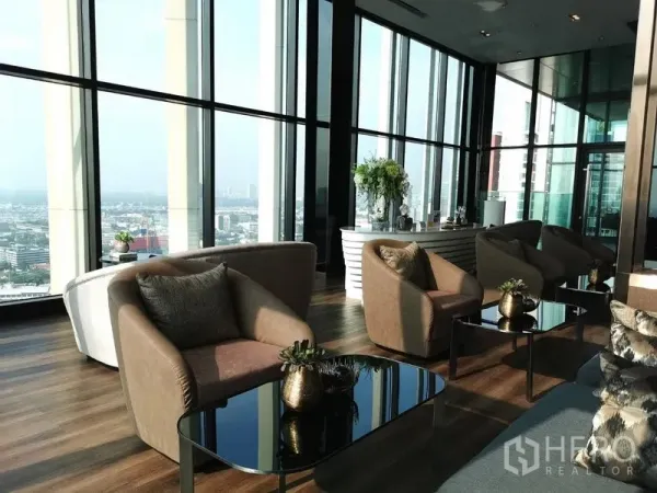 Condominium for sale in Khlong Toei, Bangkok - Sky lounge with floor-to-ceiling windows, modern armchairs, and coffee tables overlooking the city.