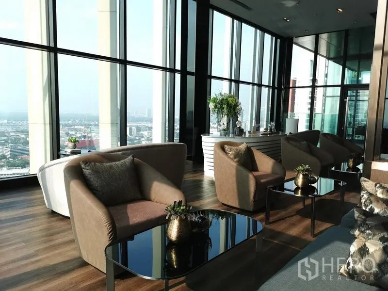 Condominium for sale in Khlong Toei, Bangkok - Sky lounge with floor-to-ceiling windows, modern armchairs, and coffee tables overlooking the city.