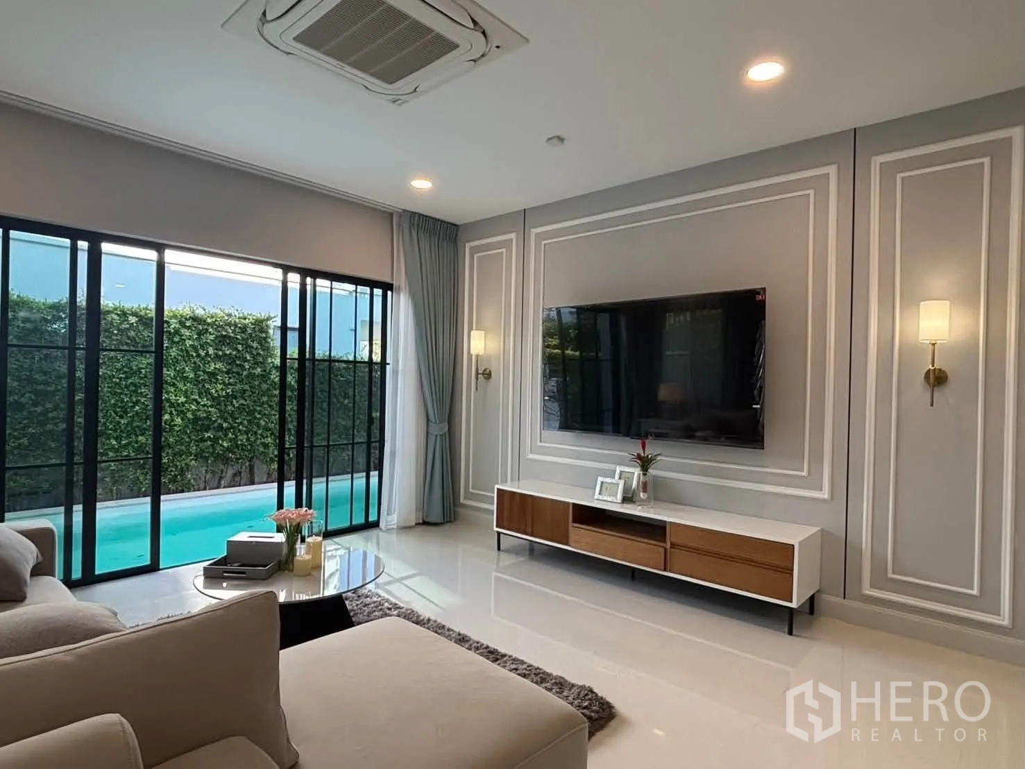 Detached House for rent in Saphan Sung, Bangkok - Living area with TV wall paneling and view of the pool and hedge garden.