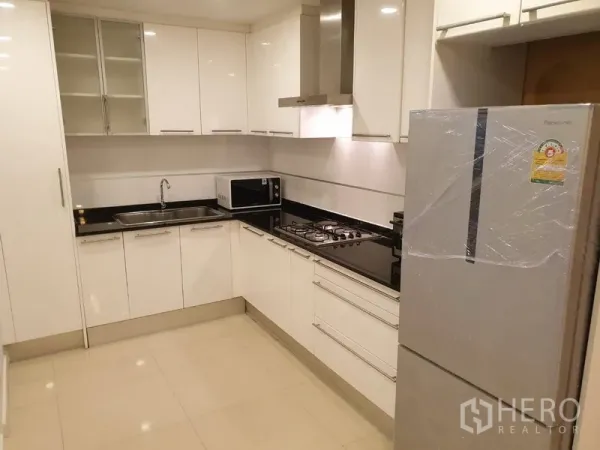 公寓 出租在Watthana, Bangkok - 现代L形白色厨房，燃气灶与抽油烟机、水槽、微波炉及大冰箱。