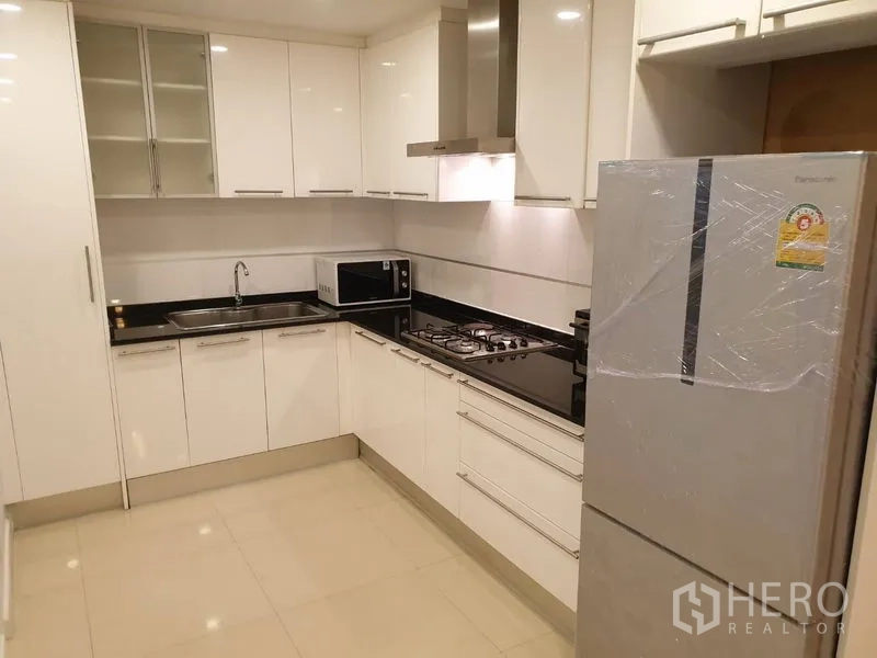 公寓 出租在Watthana, Bangkok - 现代L形白色厨房，燃气灶与抽油烟机、水槽、微波炉及大冰箱。