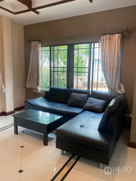 独立式住宅 出租或出售在Mueang Nonthaburi, Nonthaburi - 明亮客厅，L形黑色皮沙发、玻璃茶几与大窗。