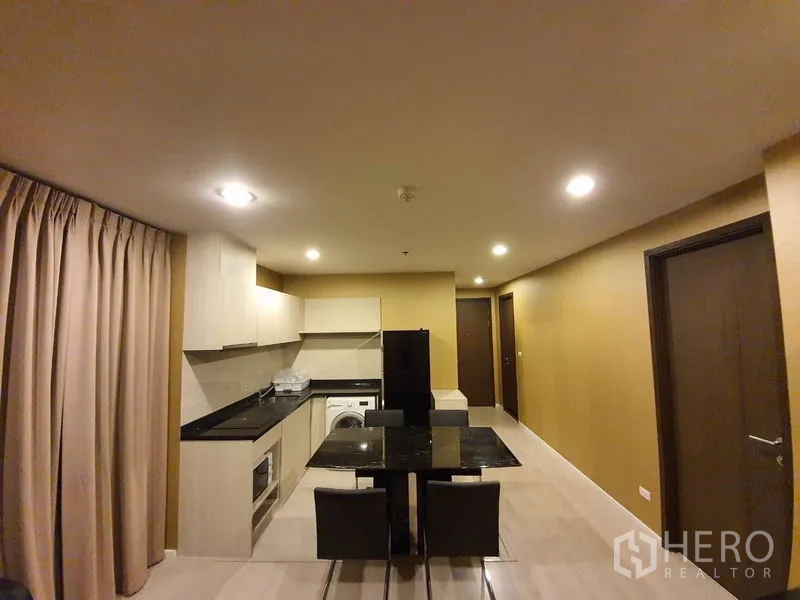 公寓 出租在Sathon, Bangkok - L形厨房，柜体充足，花岗岩台面，带洗衣机与黑色冰箱，旁为用餐区。