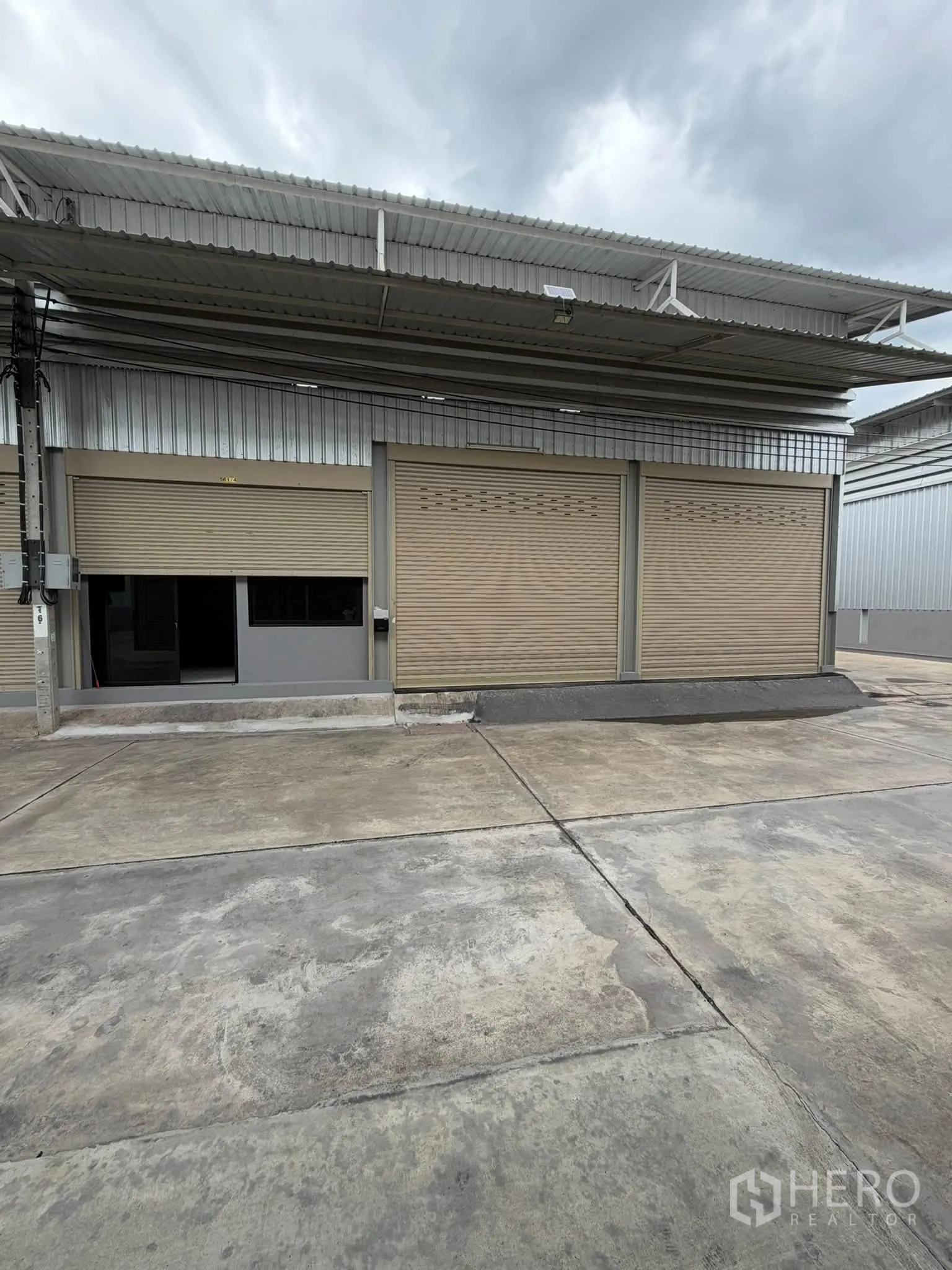 Warehouse for rent in Phra Pradaeng, Samut Prakan - Front elevation with three roller shutters and a broad driveway for truck access.