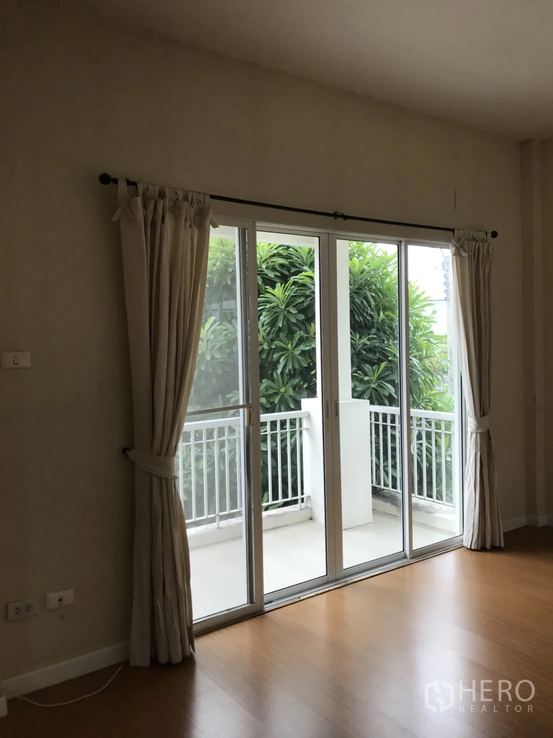 Detached House for rent in Lat Krabang, Bangkok - Bedroom with sliding glass doors to a balcony overlooking lush greenery and a white railing.