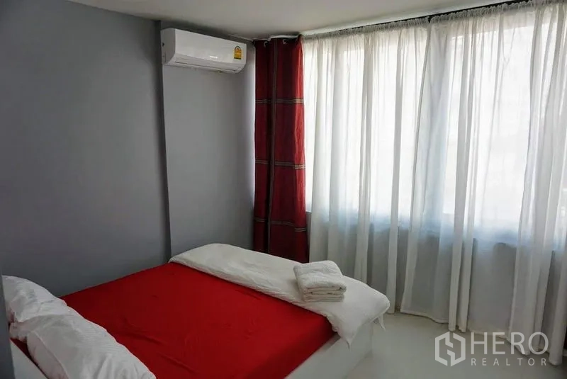 Shophouse for sale in Phra Khanong, Bangkok - Secondary bedroom with red bedding, corner air-conditioner and full-height windows.