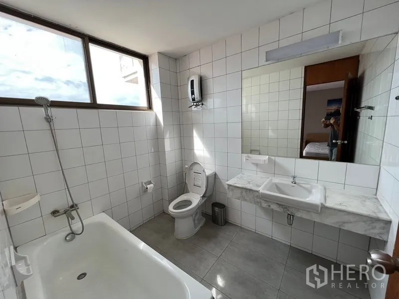 Townhouse for rent or sale in Suan Luang, Bangkok - Tiled bathroom with bathtub and shower, large mirror, toilet and natural light from the window.