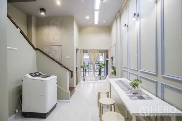 Townhouse for rent in Khlong Toei, Bangkok - Bright entry living area with high ceiling, staircase, long table and windows opening to a small terrace.