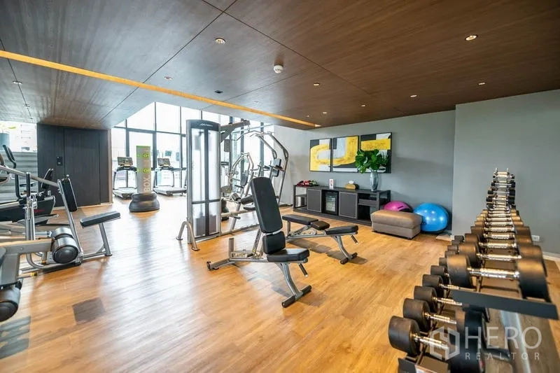 Condominium for rent or sale in Khlong Toei, Bangkok - Condominium fitness center with cardio machines, free weights and benches on wood flooring.
