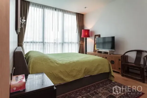 公寓 出租在Watthana, Bangkok - 卧室带落地窗，绿色床品，电视柜与柔和灯光营造舒适氛围。