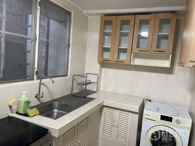 Apartment for rent in Watthana, Bangkok - Bright kitchen corner with sink, glass-front wall cabinets and a washing machine.