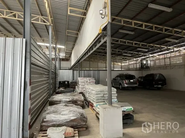 Warehouse for rent in Suan Luang, Bangkok - Covered loading and storage area with pallets and materials beside drive-in access within a Bangkok warehouse.