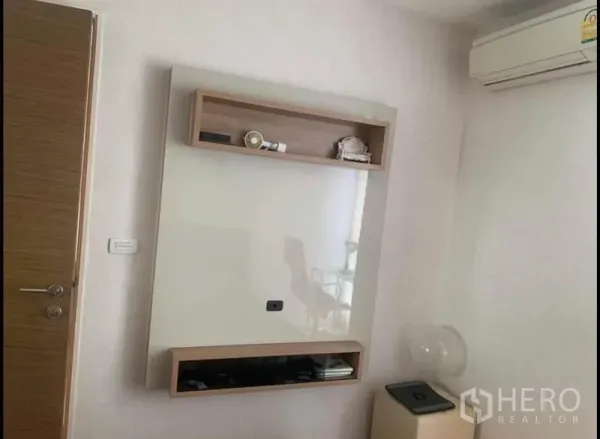 Condominium for sale in Phaya Thai, Bangkok - Wall-mounted TV panel with storage shelves and an air conditioner in a white room.