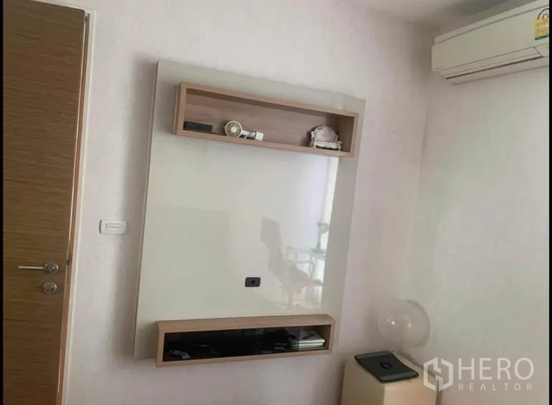 Condominium for sale in Phaya Thai, Bangkok - Wall-mounted TV panel with storage shelves and an air conditioner in a white room.