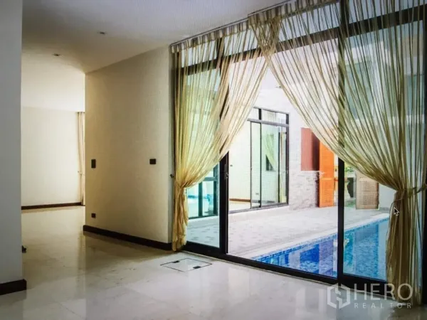 Detached House for rent in Khlong Toei, Bangkok - Bright living area with sliding glass doors and sheer curtains opening to the pool.