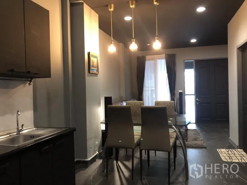 Townhouse for rent in Bang Kapi, Bangkok - Glass dining table under warm pendant lights facing the entry and curtained windows.