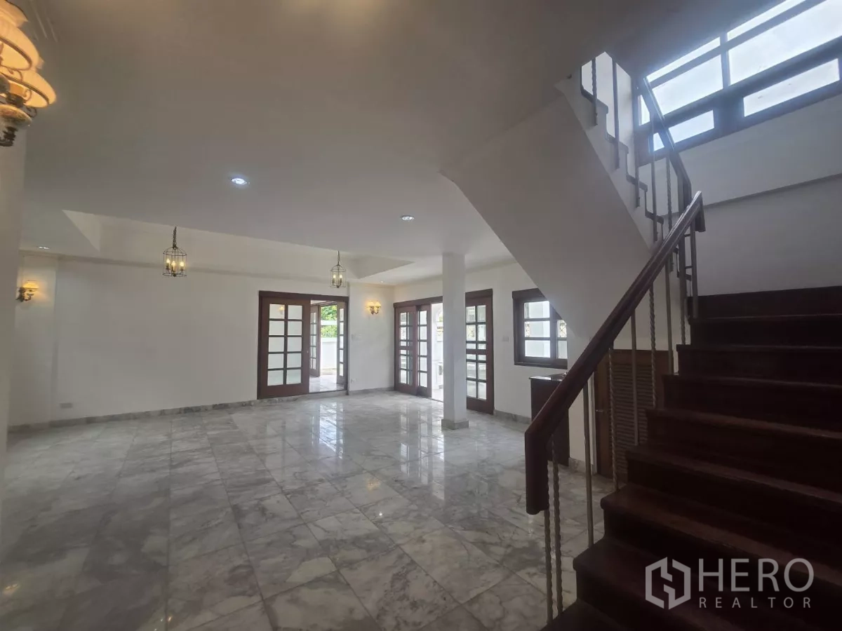 Detached House for rent in Phra Khanong, Bangkok - Living area with staircase, multiple French doors and natural light over marble flooring.