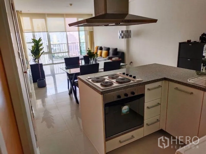 Condominium for rent in Watthana, Bangkok - Open-plan kitchen with electric cooktop and oven leading to dining and living area with skyline views.