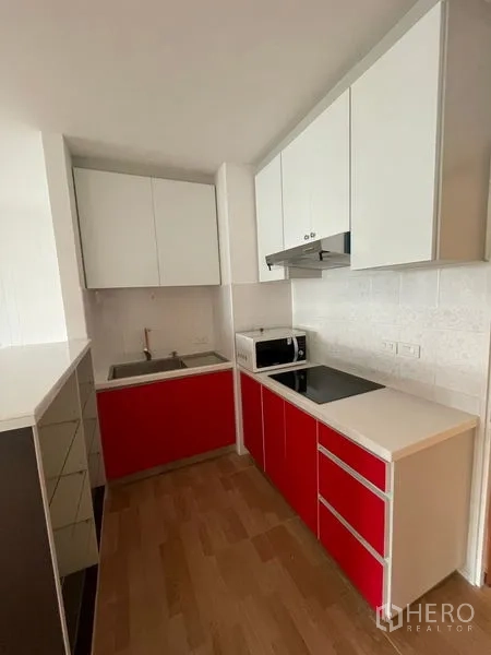 Condominium for rent in Watthana, Bangkok - Compact kitchen with red lower cabinets, hob, hood and microwave.