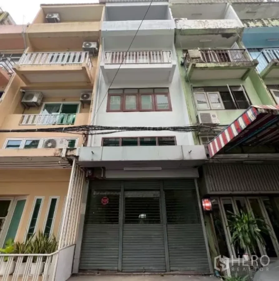 Shophouse for rent in Khlong Toei, Bangkok - Row shophouse facade with metal roller shutter and balconies in an urban lane.