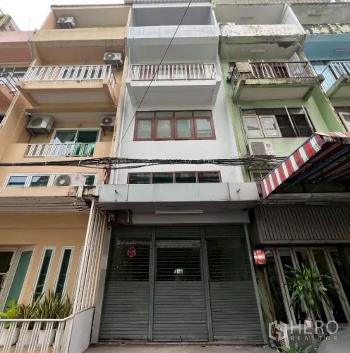 Shophouse for rent in Khlong Toei, Bangkok - Row shophouse facade with metal roller shutter and balconies in an urban lane.