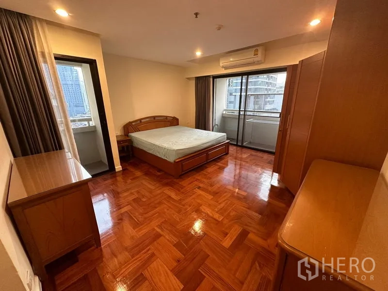 公寓 出租在Watthana, Bangkok - 宽敞卧室铺设人字木地板，木质床与储物柜，落地推拉门连通城市景观阳台。