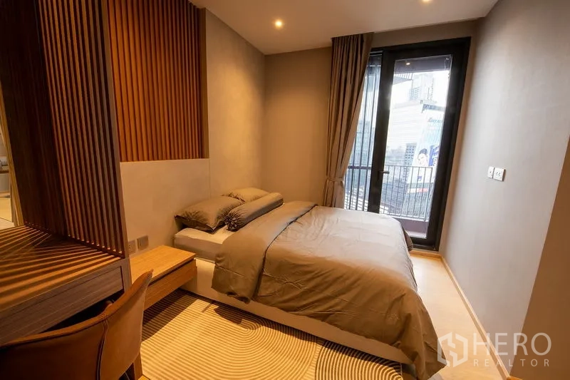 Condominium for rent in Din Daeng, Bangkok - Warm bedroom with double bed, wood slat headboard and glass door to a small balcony overlooking the city.
